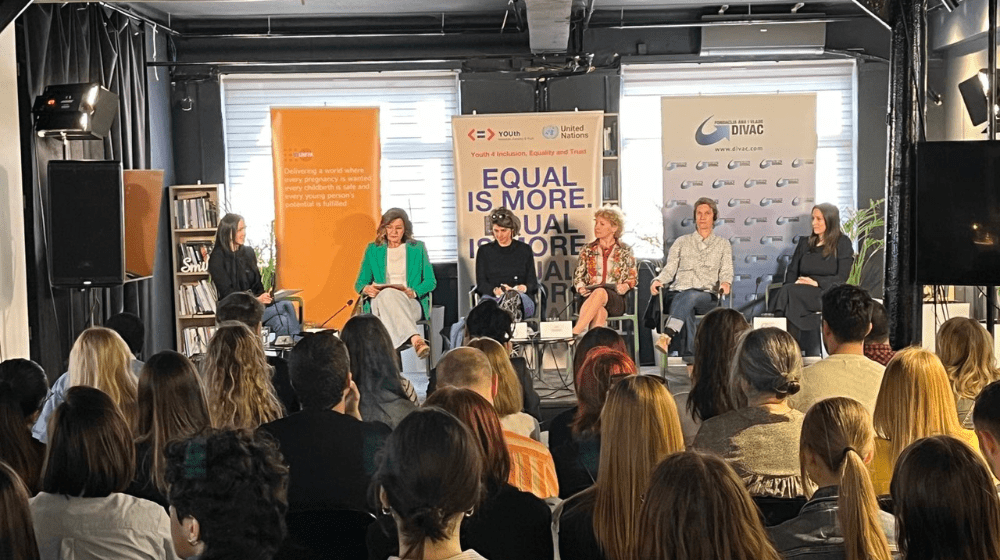 5 women sitting at the center, audience around