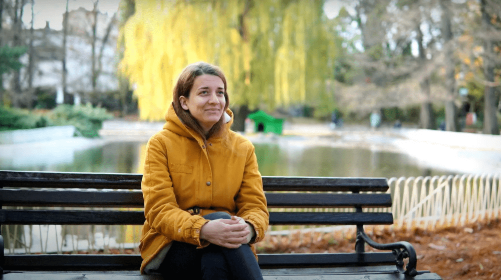 Maja, a graduate student at the Academy of Arts in Novi Sad, Serbia, sitting on a bench in a park.