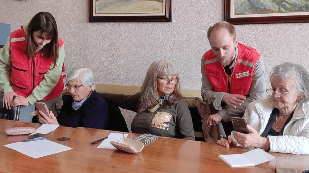 Two Red Cross officers assist three older women with their phones in a supportive setting